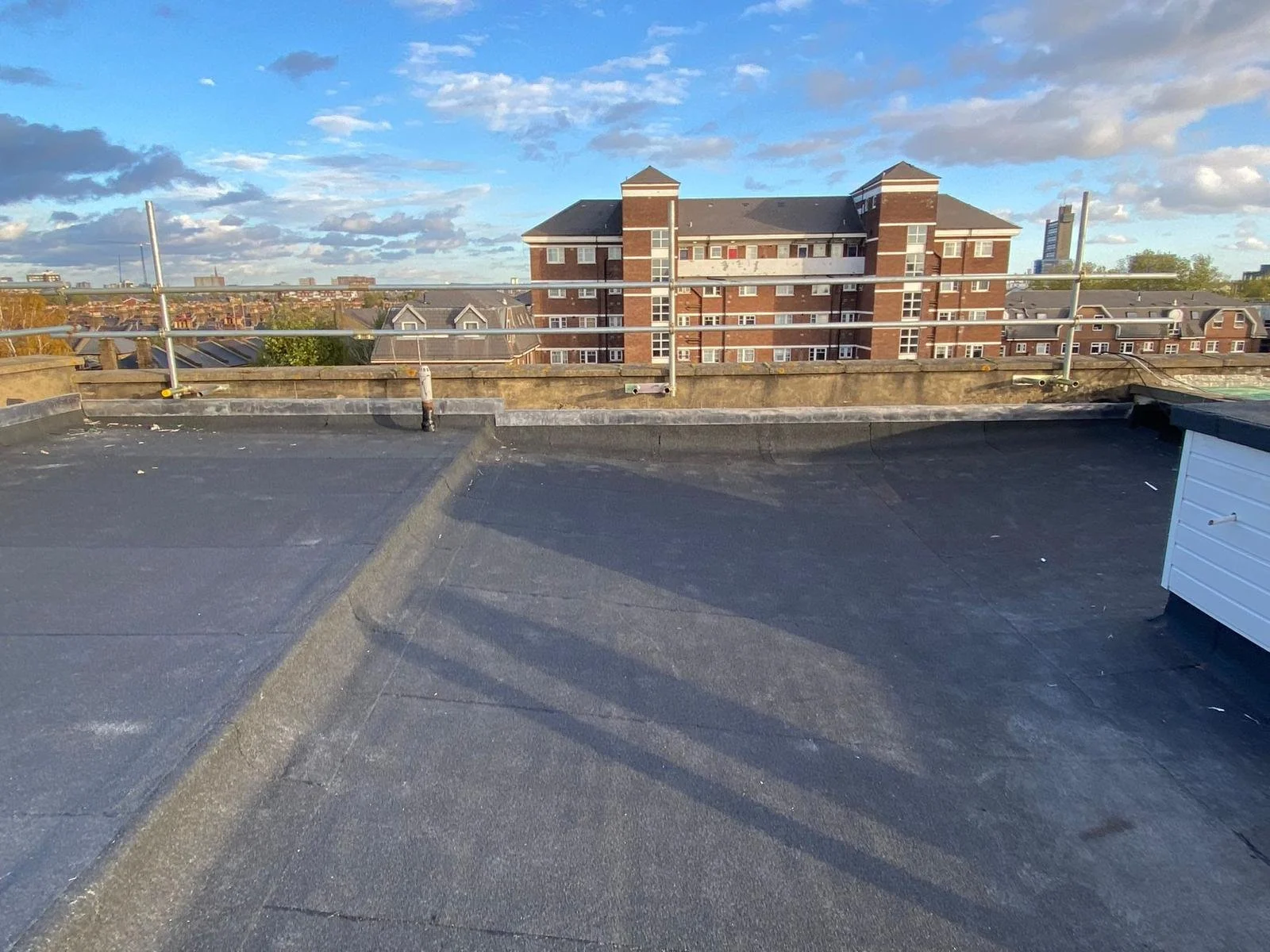 View from a rooftop with a black flat surface, railing, and a distant city skyline under a partly cloudy sky.
