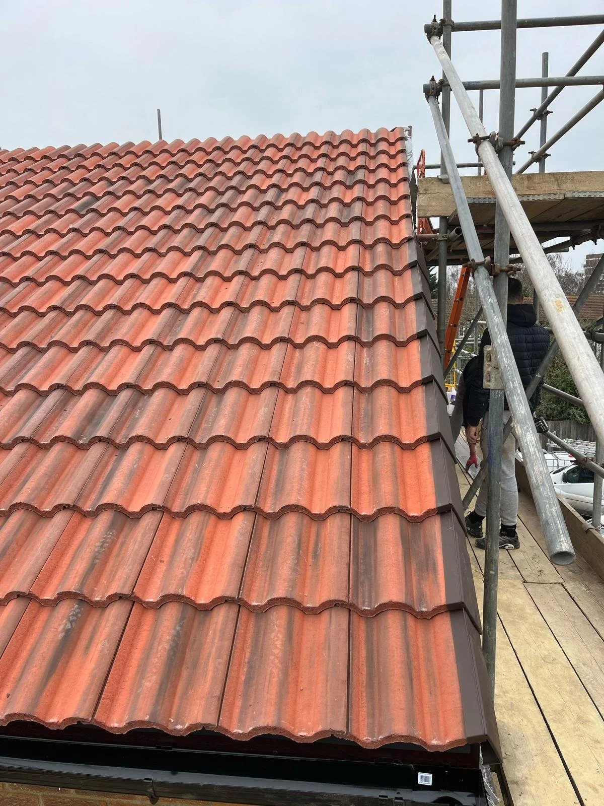 A roof under construction with red clay tiles and scaffolding on the side, with workers installing the tiles.