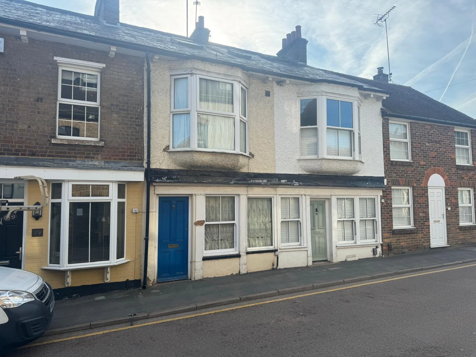 Row of attached houses with brick and stucco facades, two with bay windows, and a car parked on the street in front.