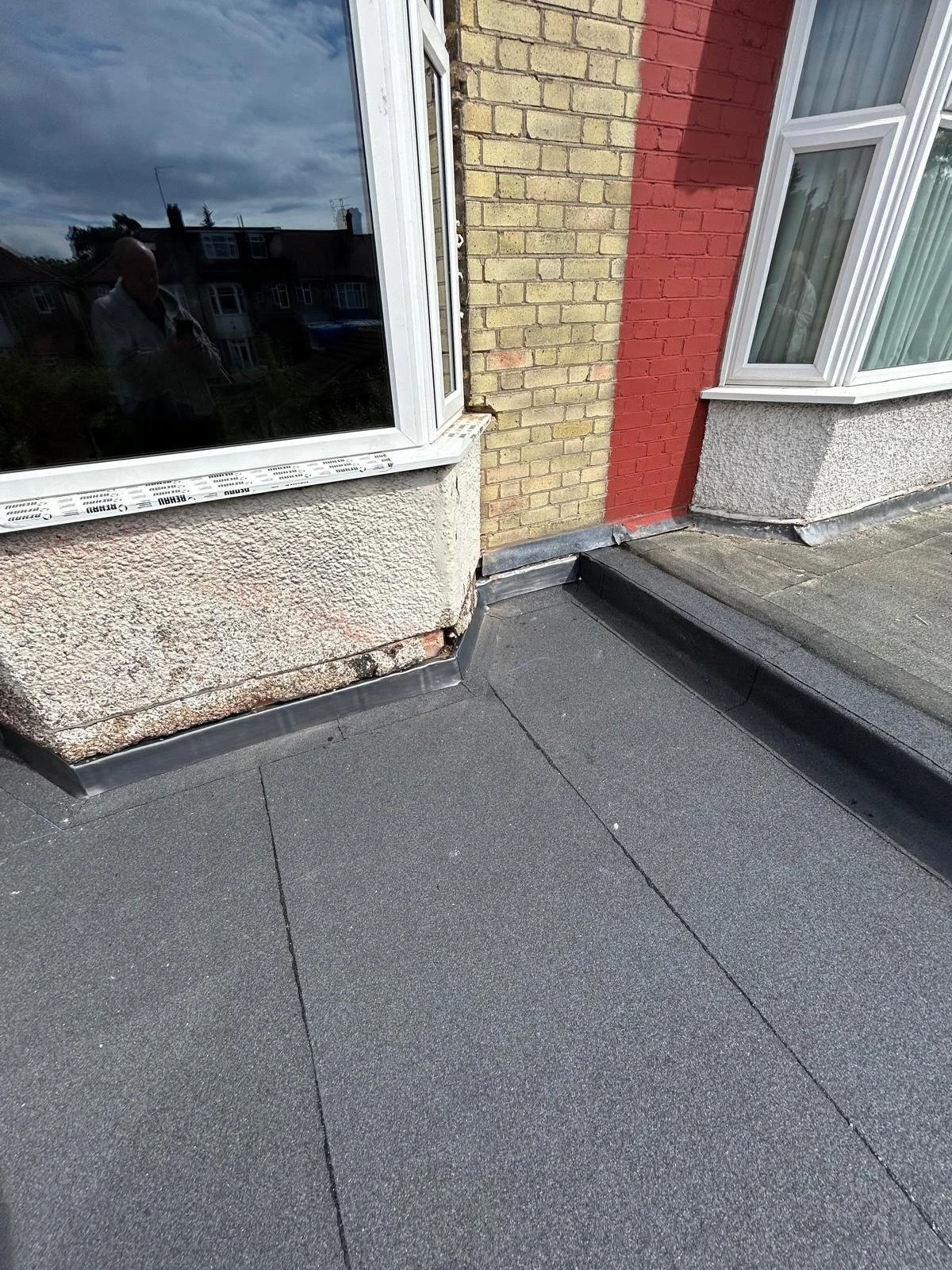 Close-up of a building exterior with new black roofing material, windows, and brick and stucco walls.