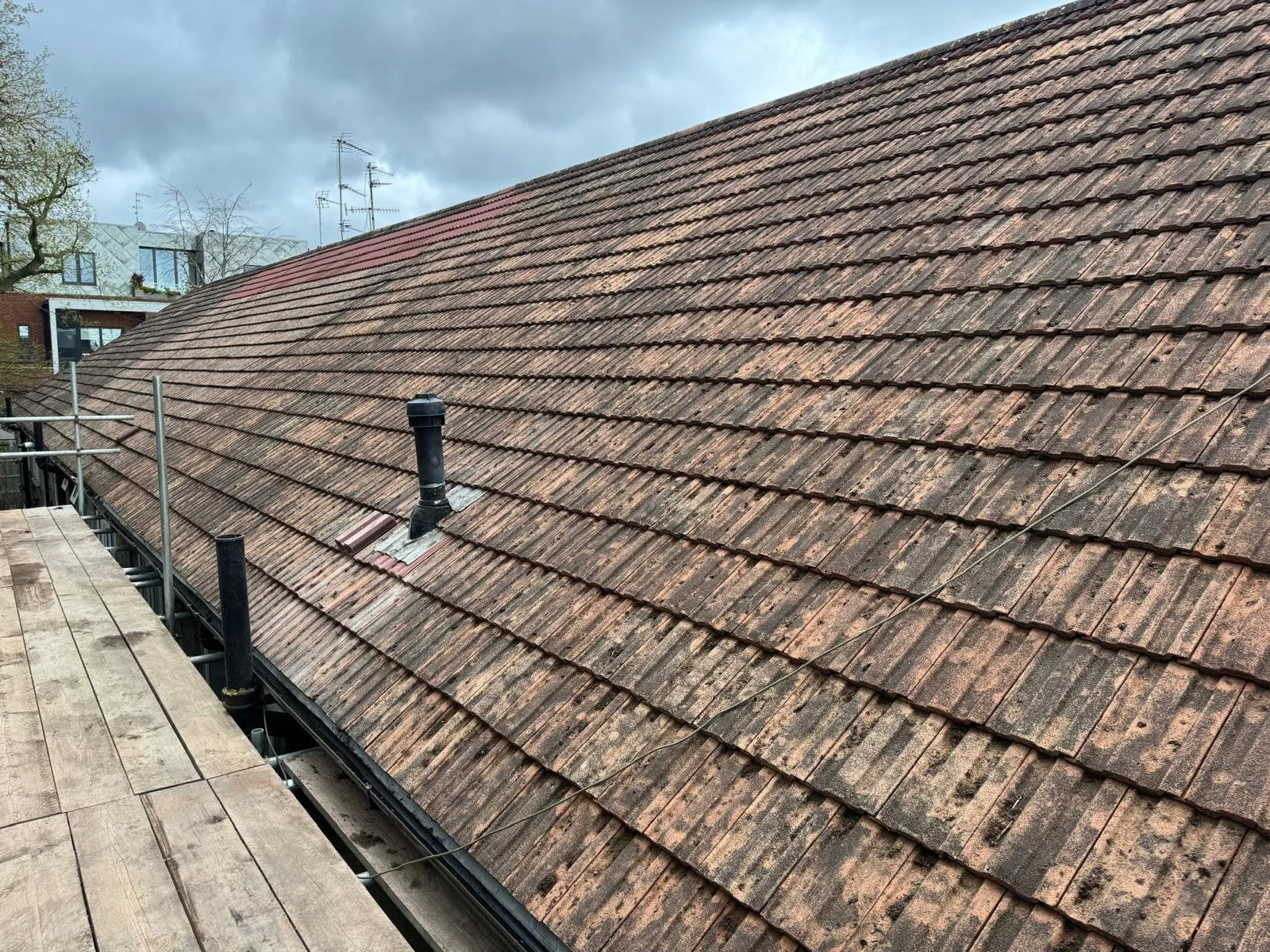 A sloped roof covered with weathered reddish-brown tiles, with two black ventilation pipes protruding. The sky above is cloudy and dark.