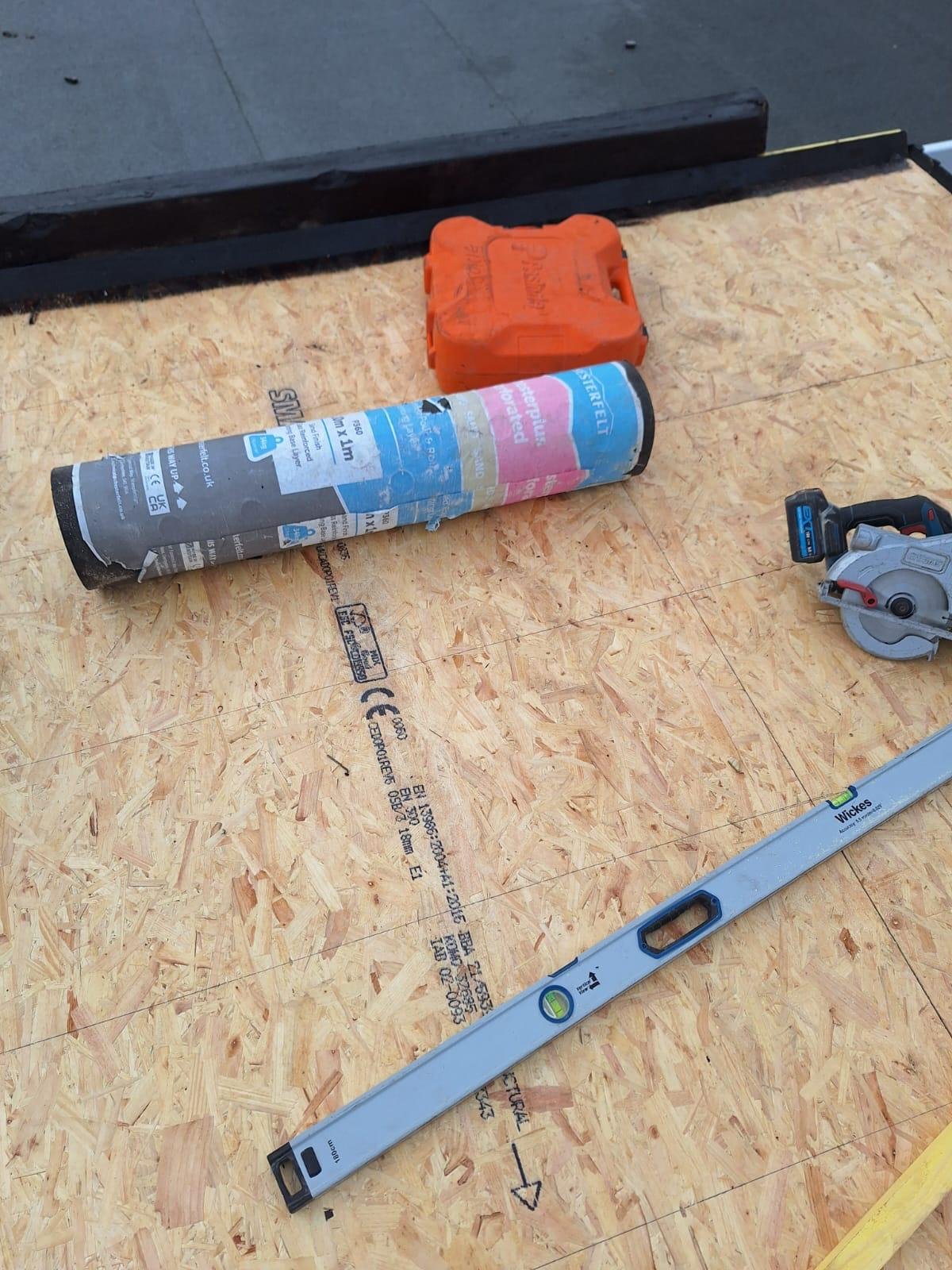 Construction site with plywood floor, a level, circular saw, a glue tube, and an orange toolbox.