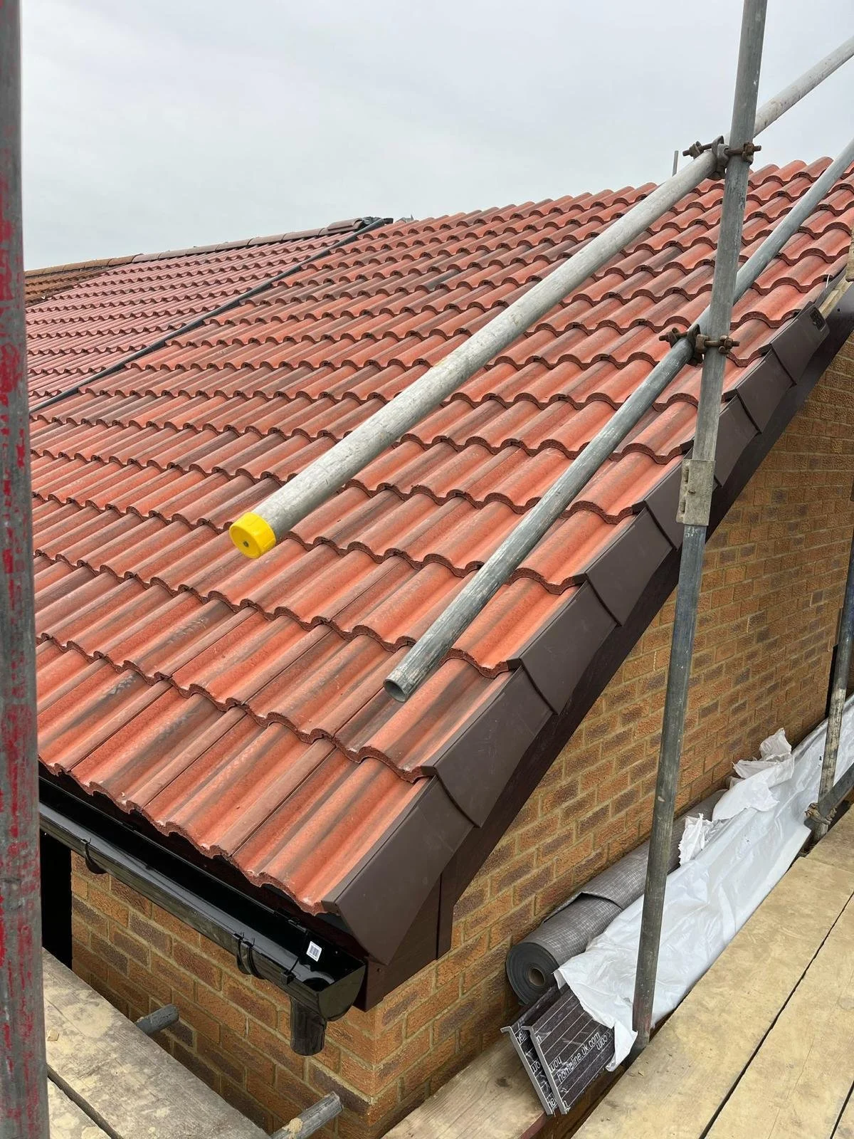 Construction scaffolding around a brick house with a new red-orange tiled roof.