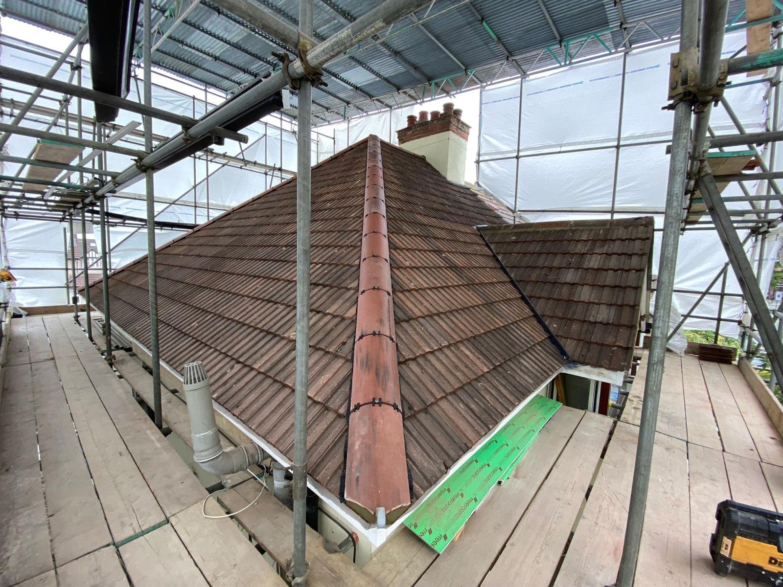 Roof of a house under construction with brown tiles, scaffolding surrounding it, and a chimney visible at the top.