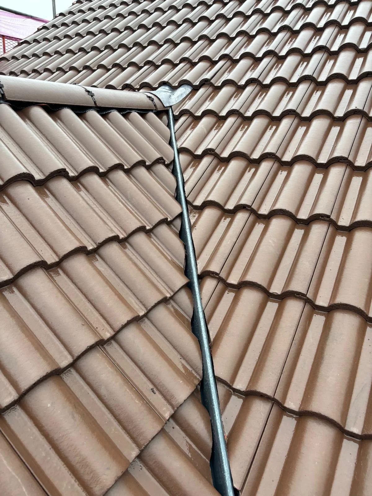 Close-up view of a brown tiled roof with a metal tool fixing a flashing on the roof.