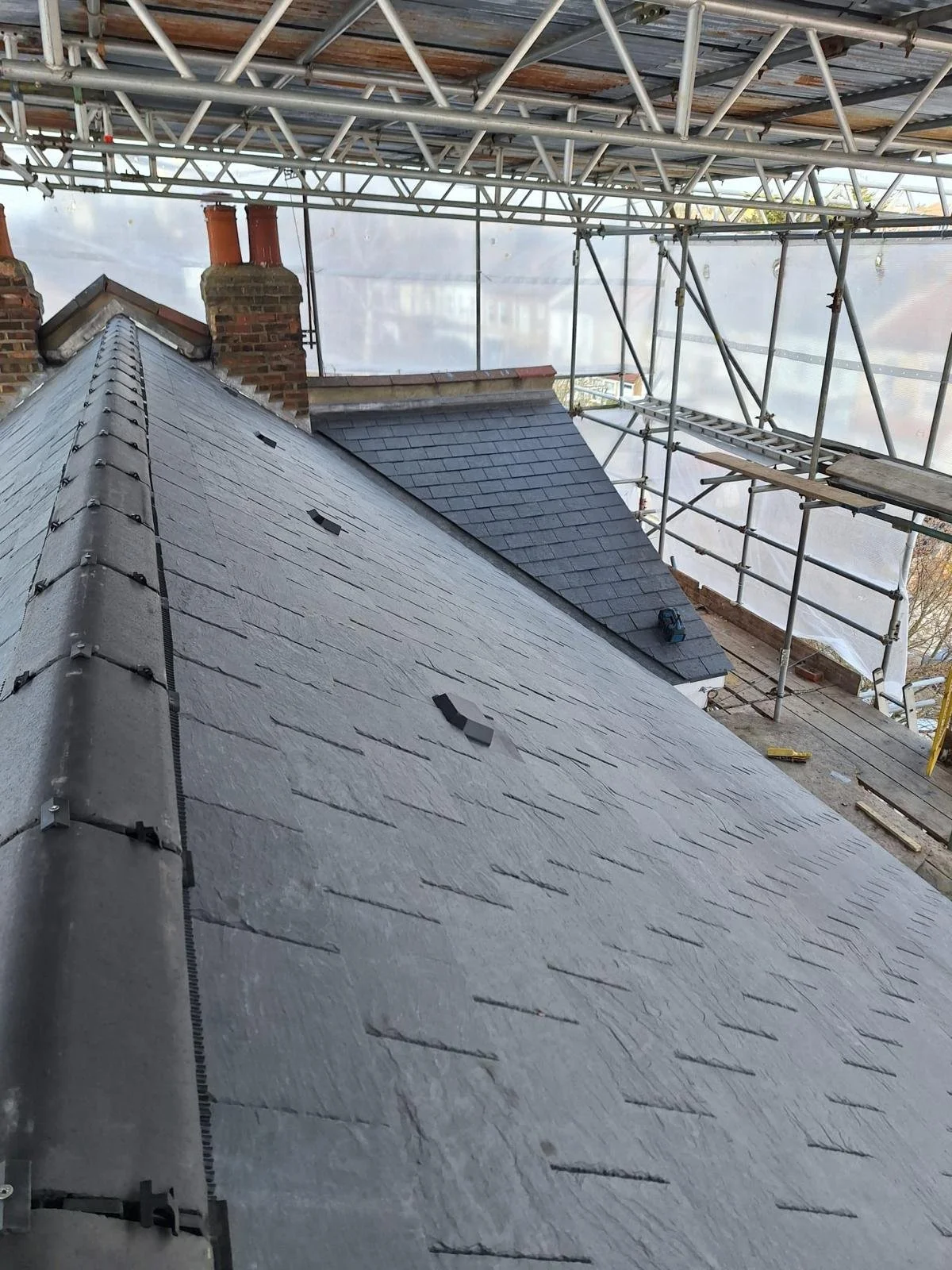 View of a residential roof with slate tiles, surrounded by scaffolding, indicating ongoing construction or repair work.