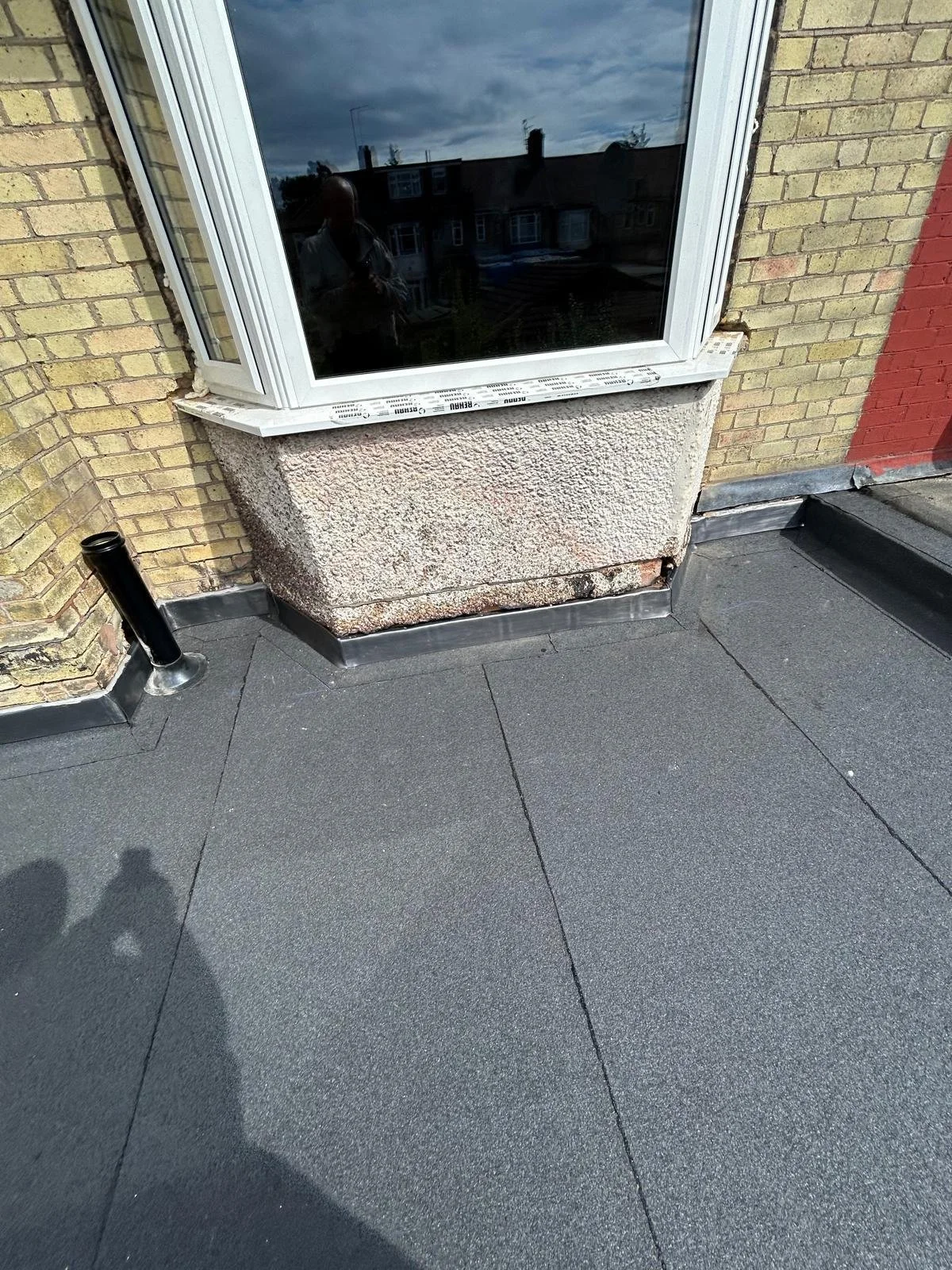 Various roofing materials on a building's exterior wall, including black roofing membrane and flashing near a window with a textured exterior wall.