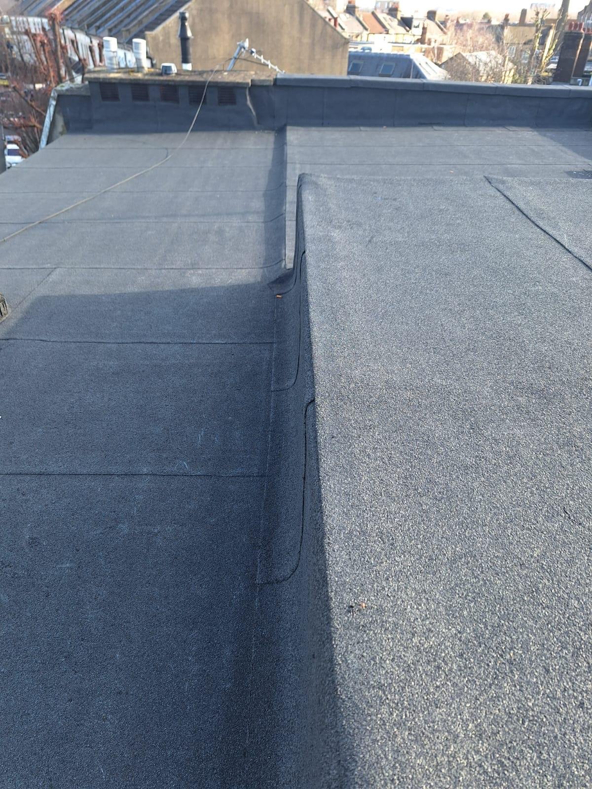 View of a rooftop with asphalt shingles, showing the seam and the edge where two sections meet, with other buildings and rooftops in the background.
