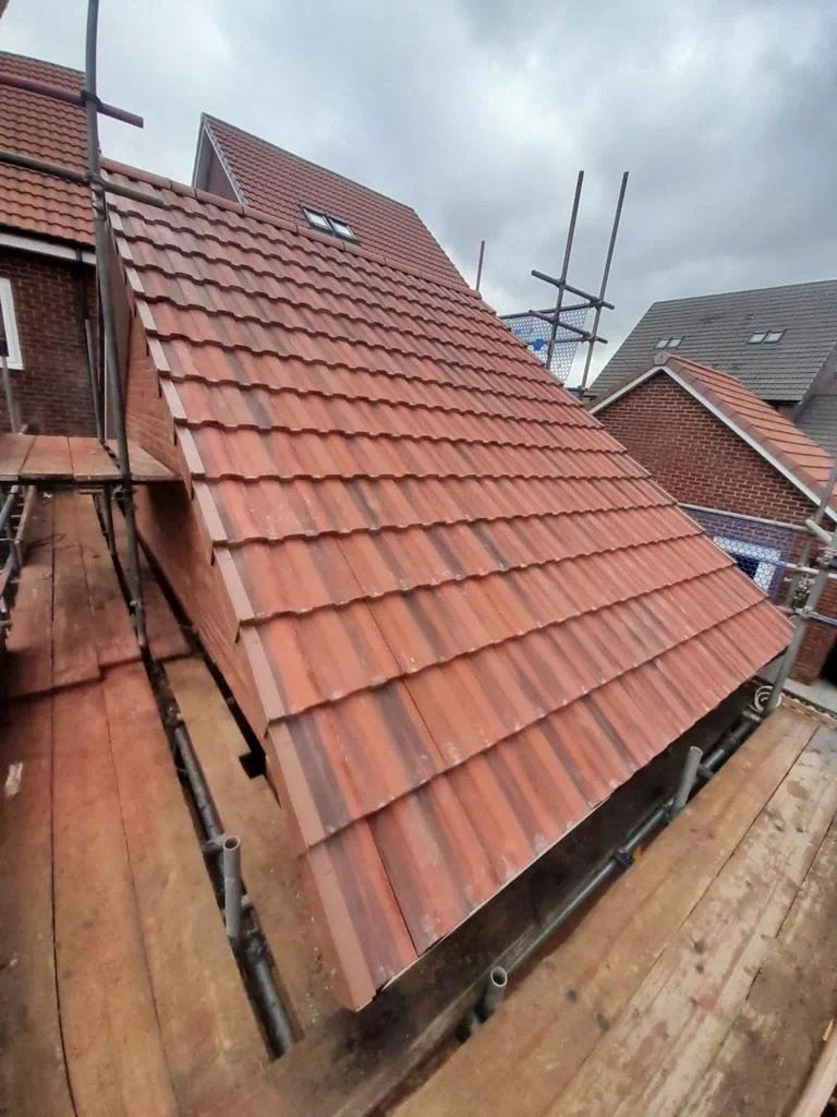Newly installed red clay roof tiles on a house under construction with scaffolding and a cloudy sky.