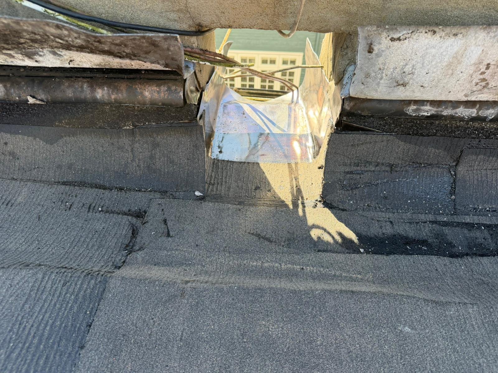 View of a roof with a damaged vent flashing and roofing materials, showing broken and bent metal parts with some exposed areas.