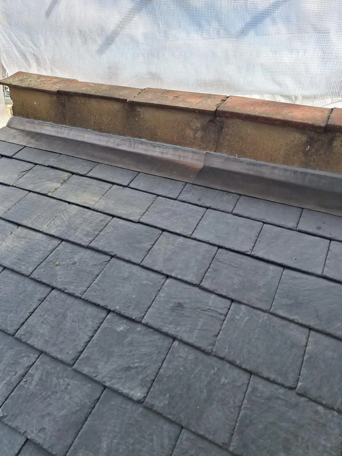 Close-up of a shingled roof with a metal flashing and brick chimney cap.