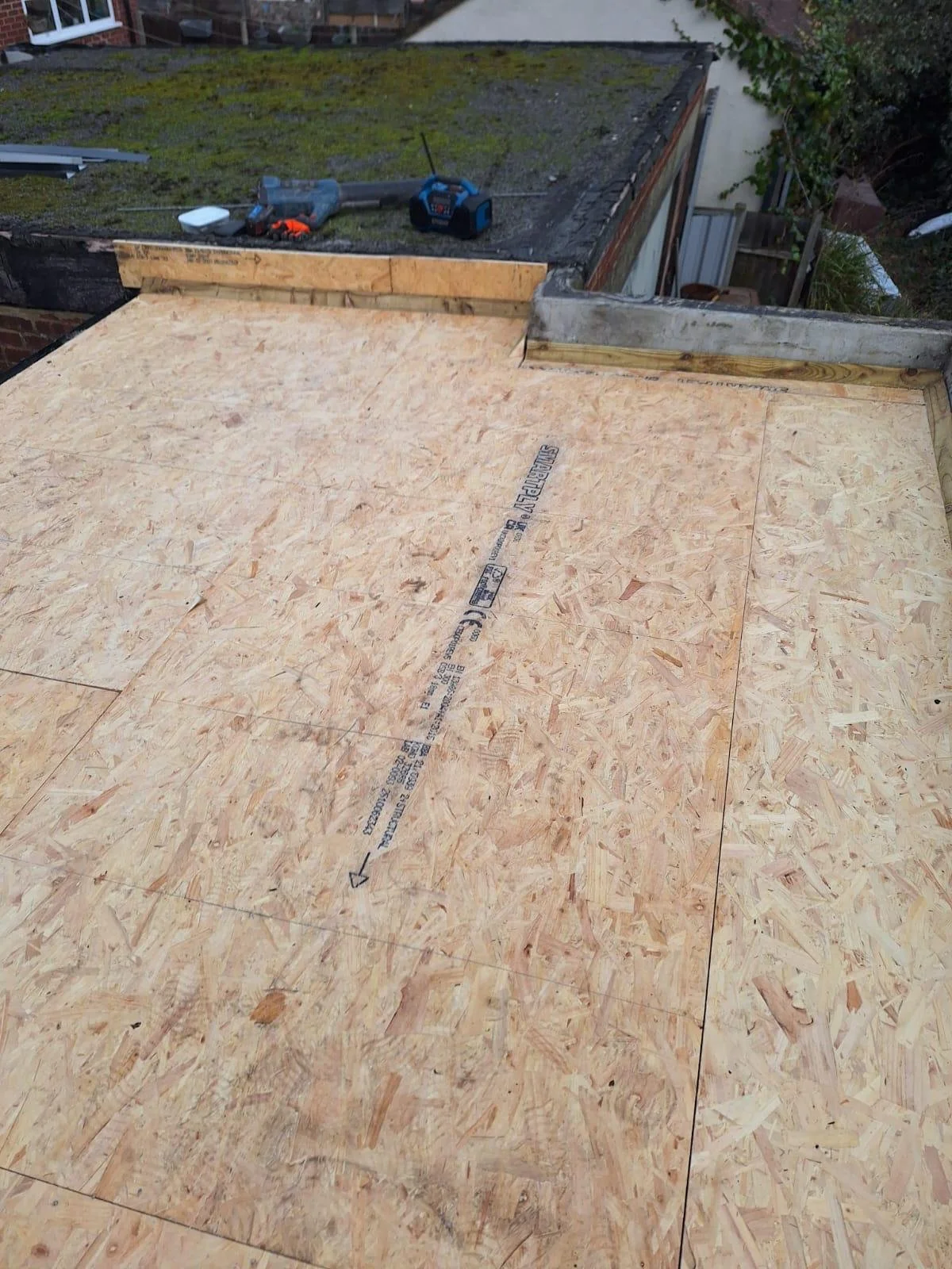 Construction site with new plywood flooring installed on a roof, with tools and equipment in the background.