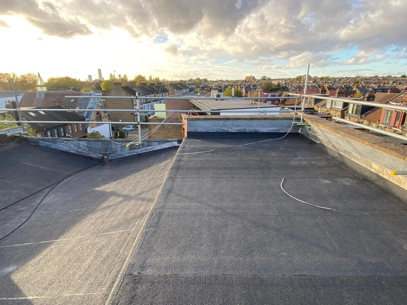 Rooftop view showing a cityscape with multiple rooftops and a sky with clouds and sunlight.