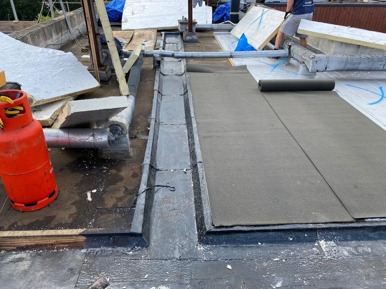A construction site on a rooftop with insulation, pipes, and roofing materials being installed.