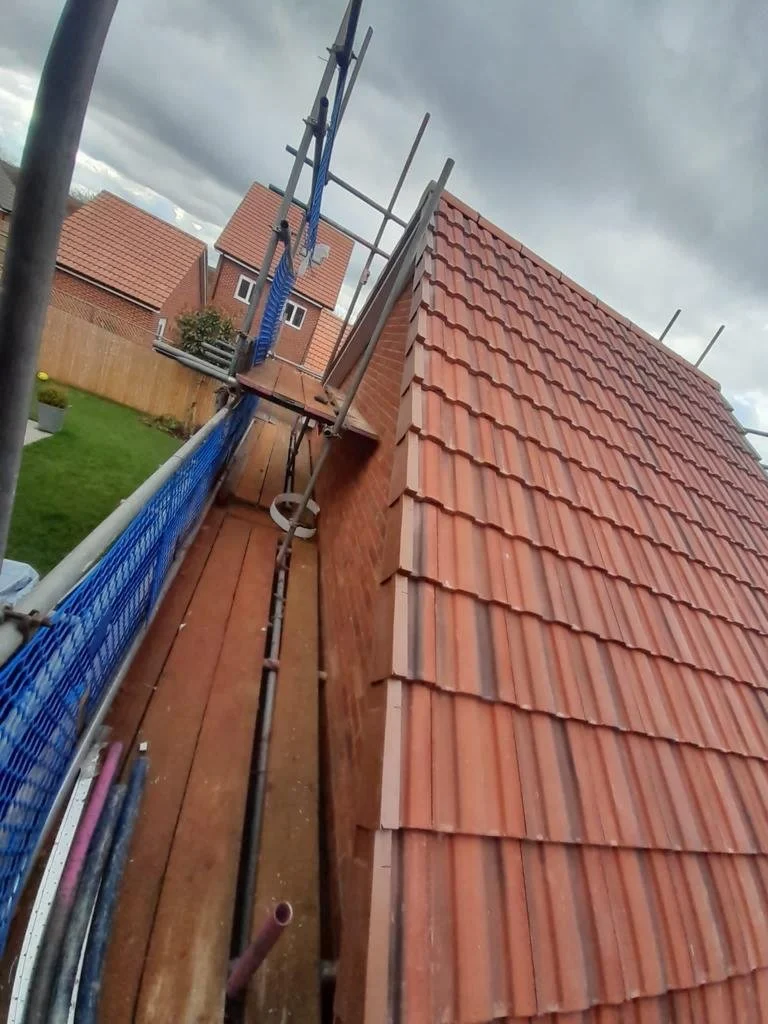 View of a roof under construction with scaffolding, orange roof tiles, and a cloudy sky.