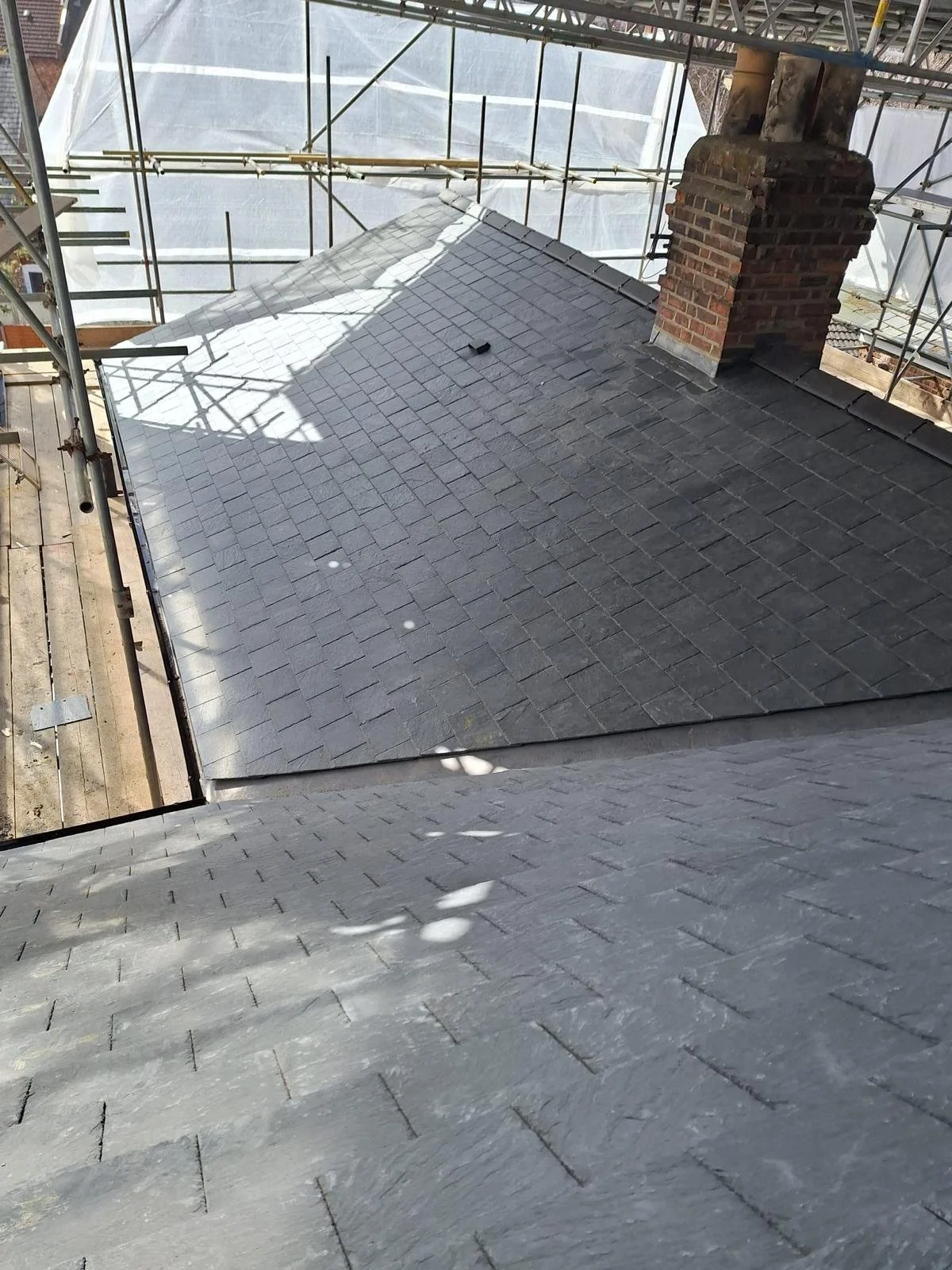 View of a slate shingle roof with scaffolding around the building and a brick chimney.