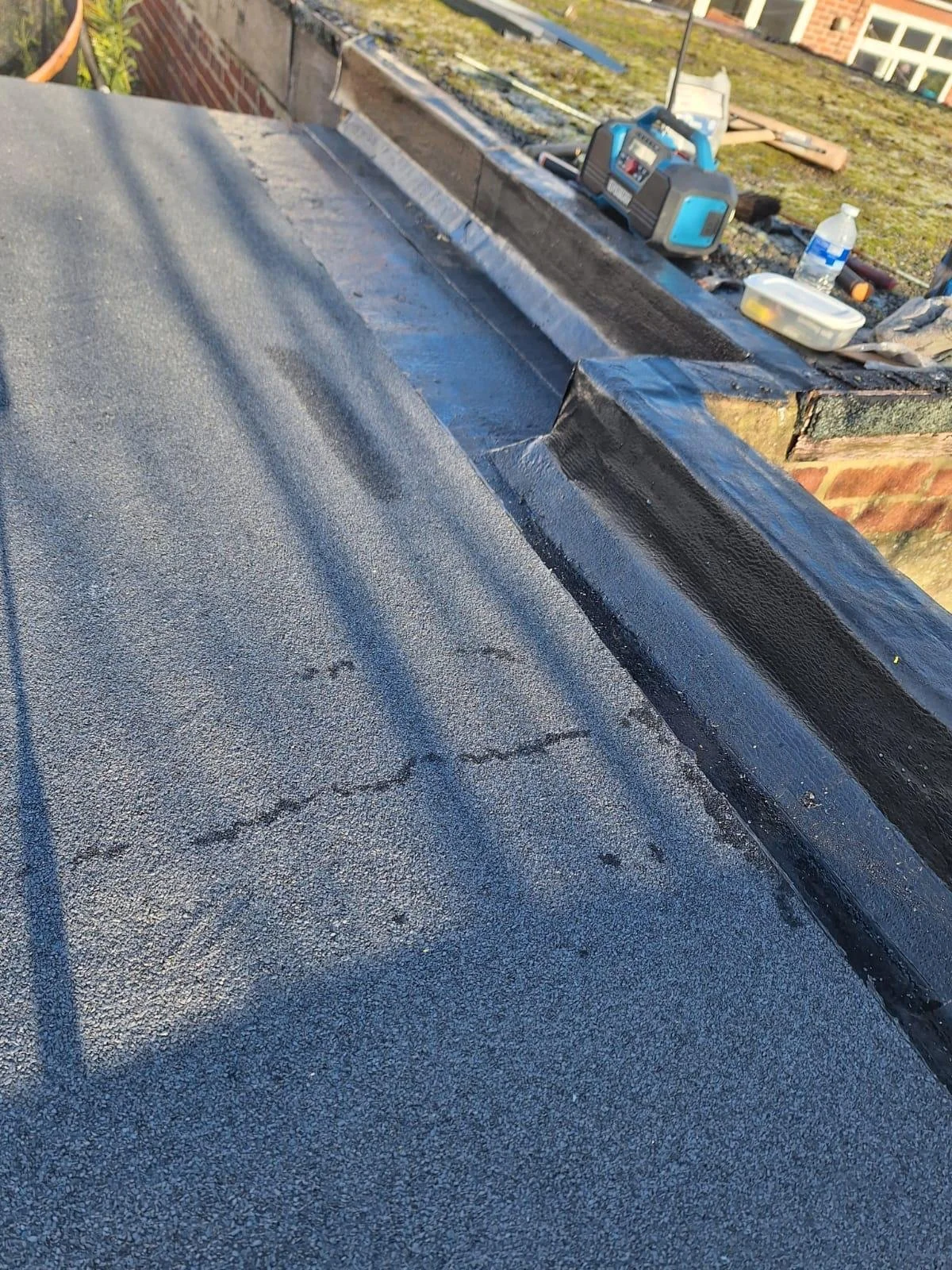 Close-up of a roof with a new black waterproofing membrane installed, with tools and materials in the background.