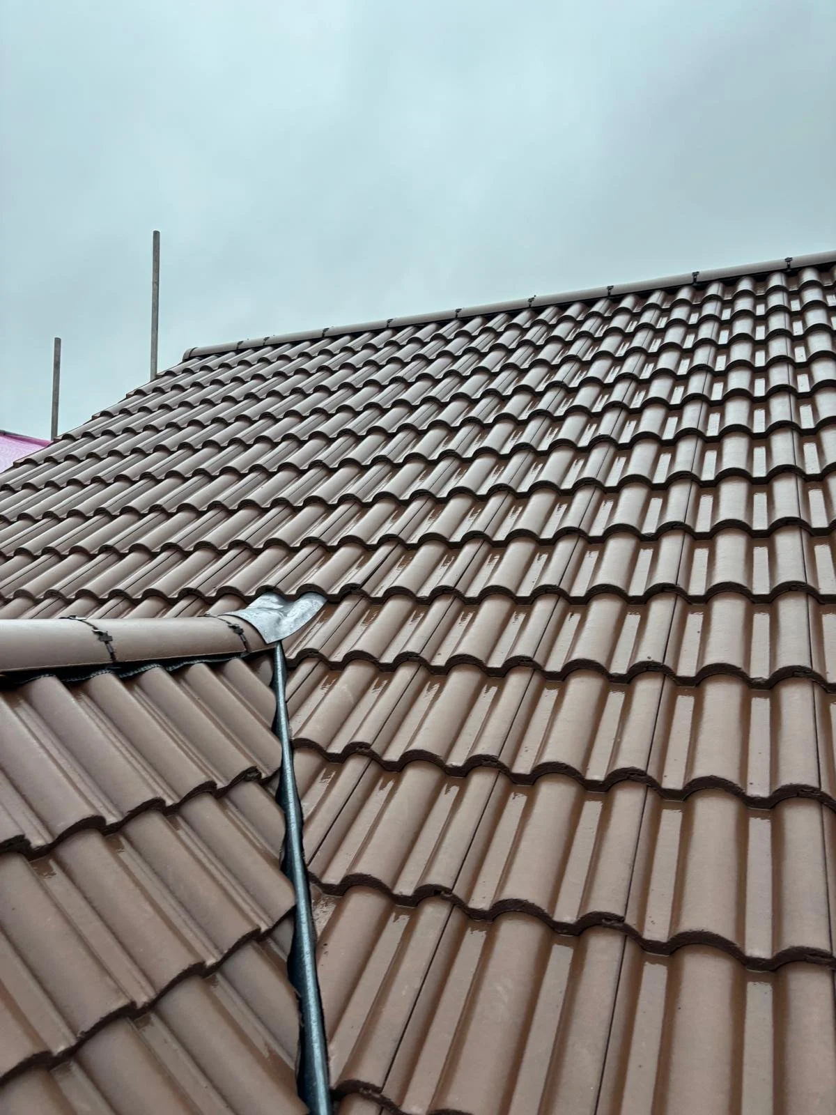 Close-up of a metal house roof with brown ceramic tiles under an overcast sky.