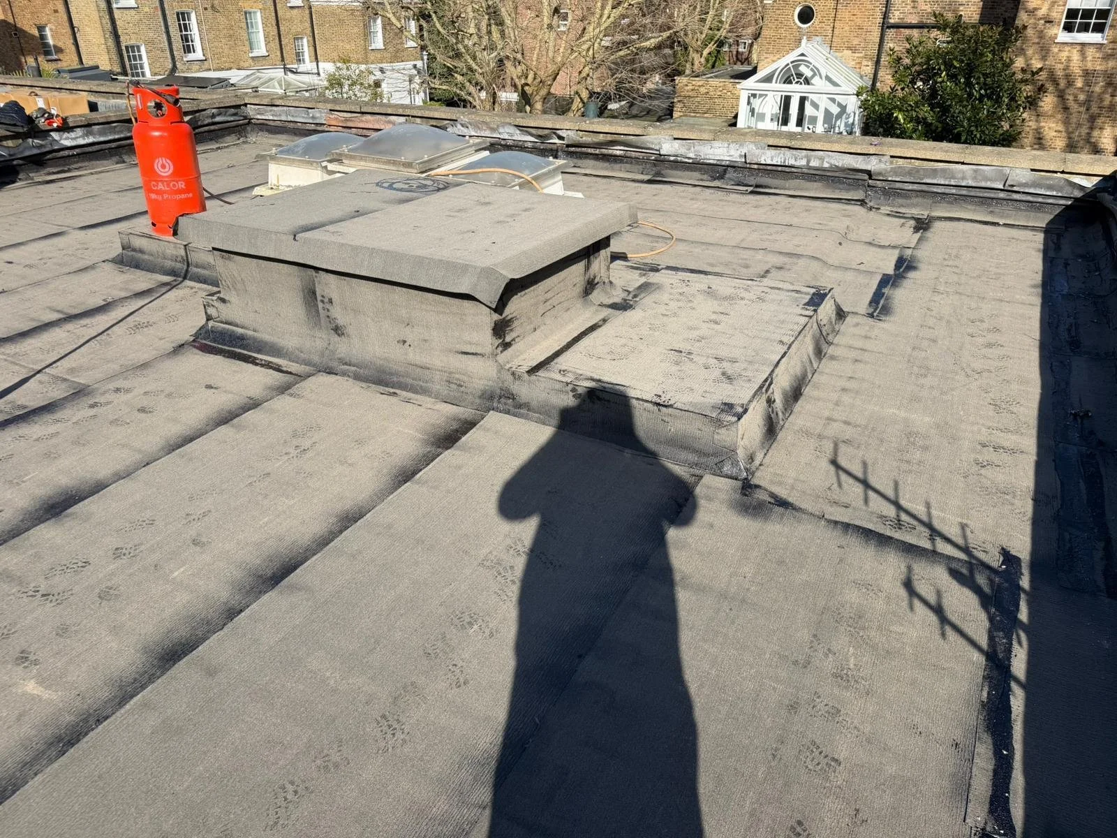 Roof with vent pipe, skylight, and tar paper, with a shadow of a person taking the photo.