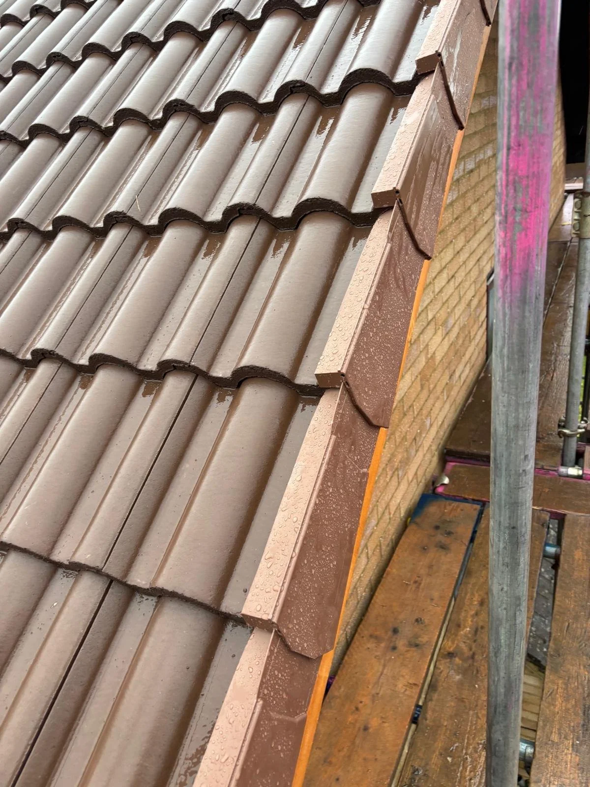 Close-up view of a newly installed brown tiled roof on a brick building, showing rain droplets on the tiles.