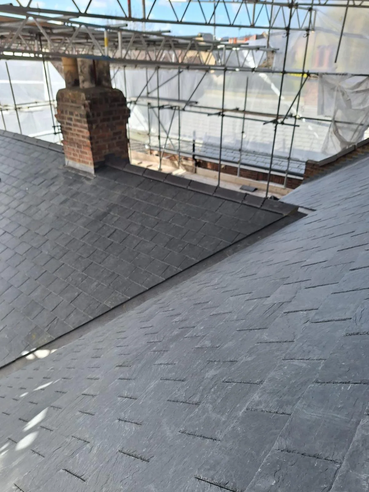 View of a house roof under construction, with scaffolding around a chimney and part of the roof covered with shingles.