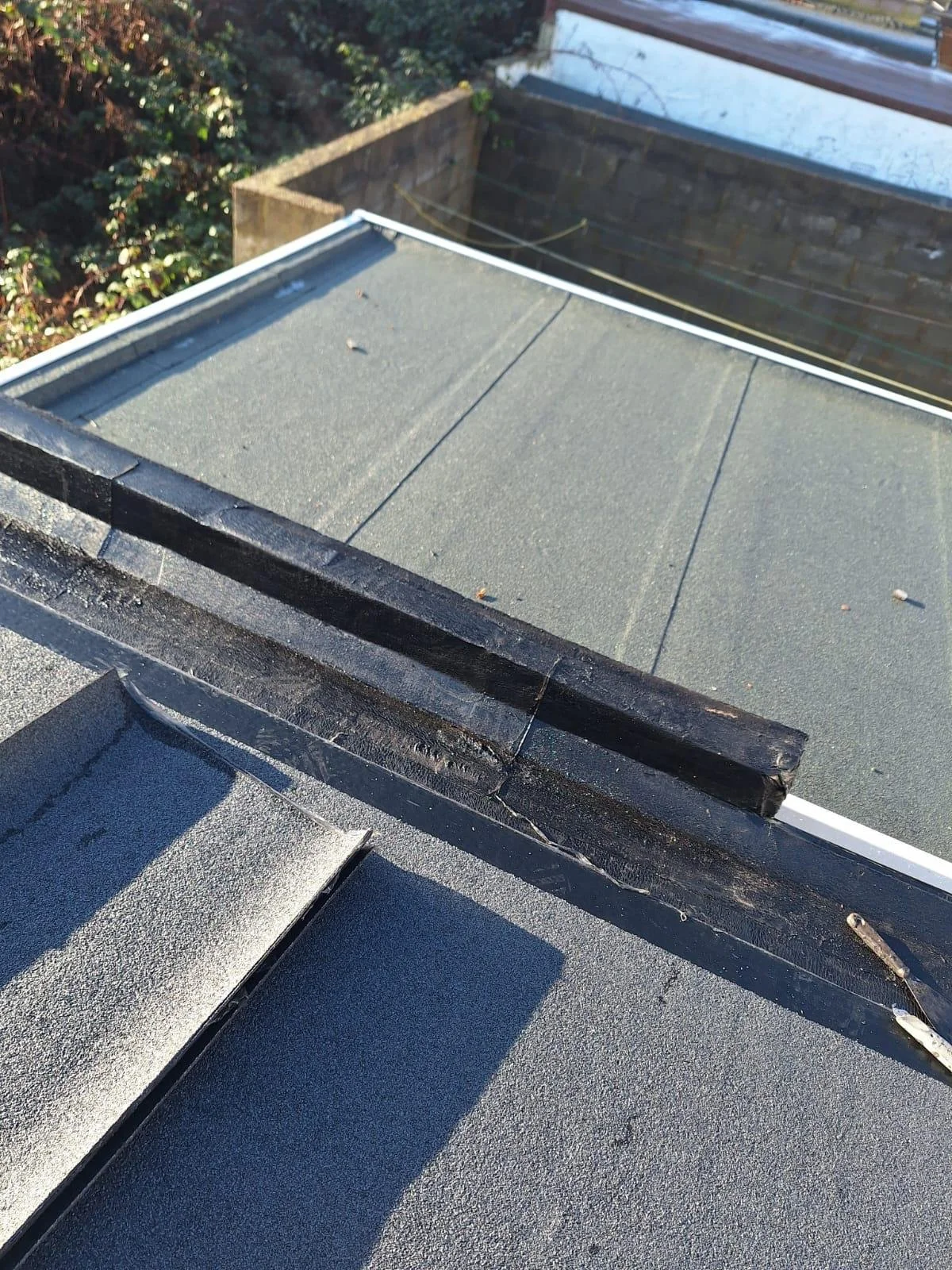 Close-up image of a roof repair Maida Vale edge showing metal flashing and asphalt shingles, with some dirt and debris.