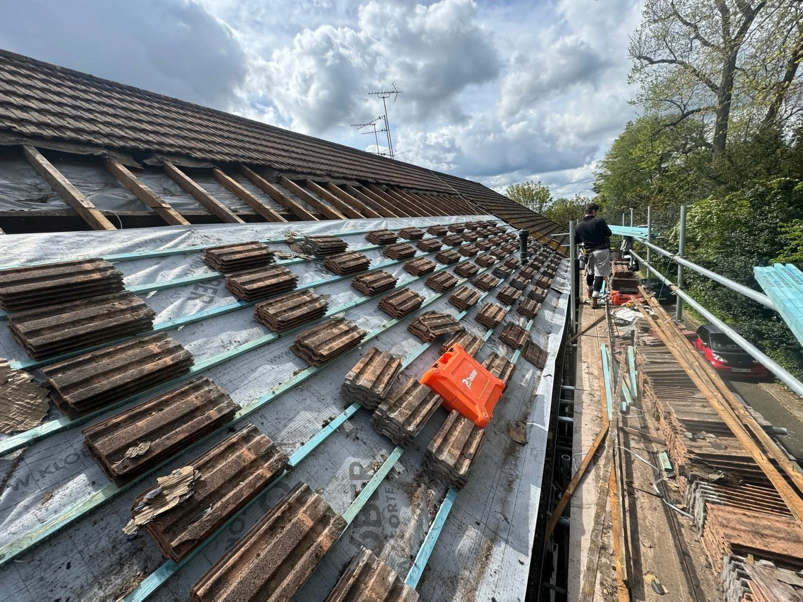 Workers are replacing roof tiles on a house with scaffolding and tools, overcast sky in the background.