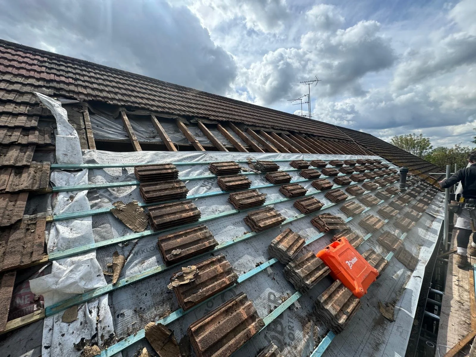 Roof under renovation with old tiles removed, new tiles being installed, and building materials and tools visible.