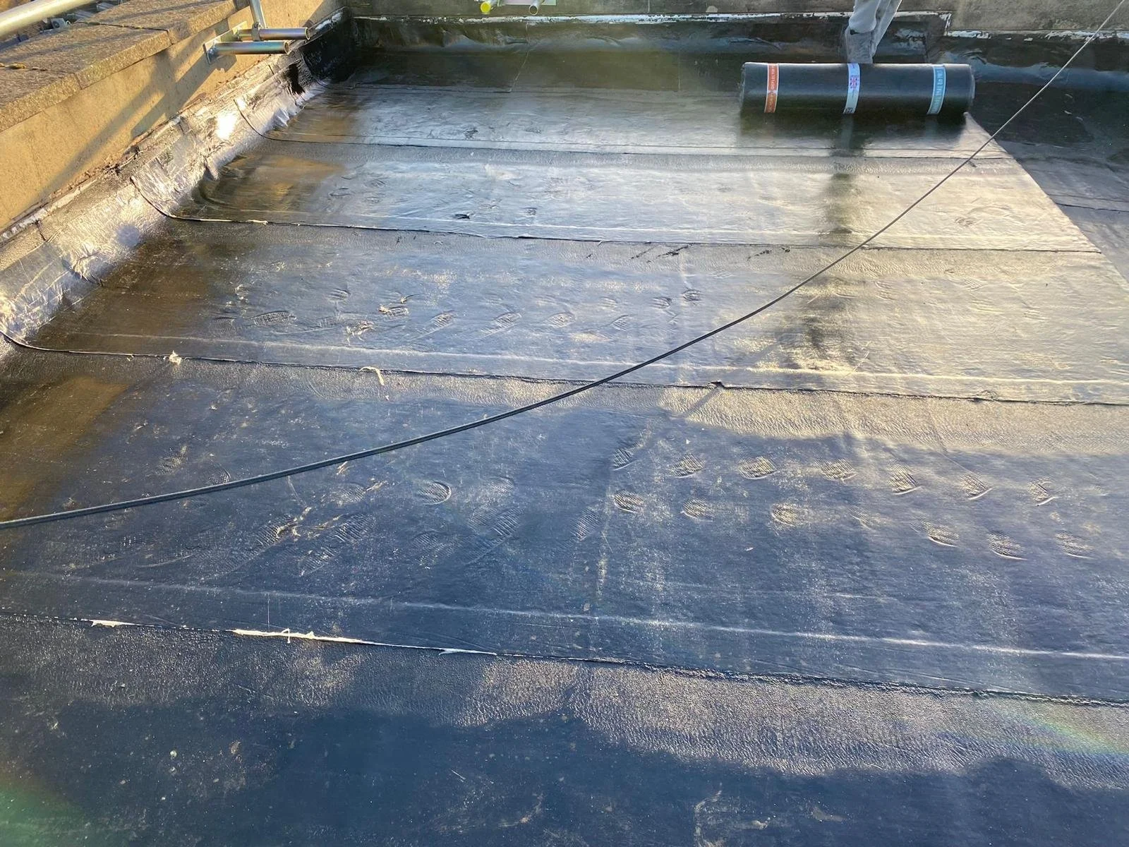 Roof covered with black waterproof material, with tools and a roll of liner in the background.