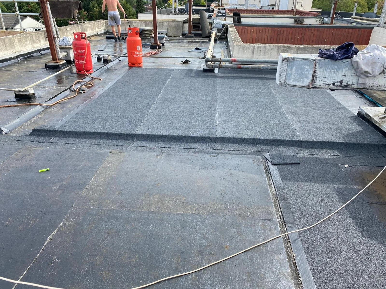 Roof construction with workers installing new roofing material, safety equipment, and tools scattered around.