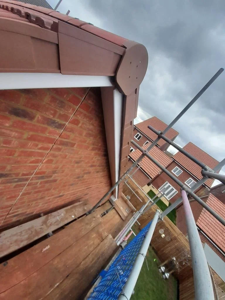 View from the side of a residential house with scaffolding, brick wall, and Maida Vale roof with brown tiles. Overcast sky.