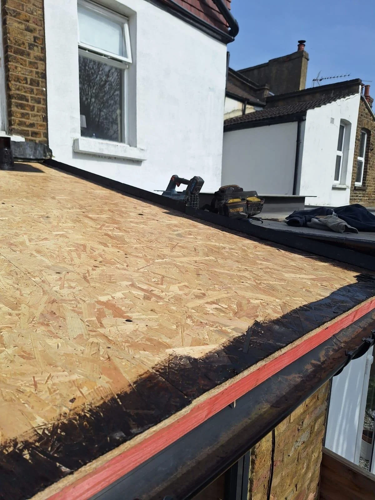 Construction on a building's roof, with plywood sheathing and tools reflecting ongoing roofing work.