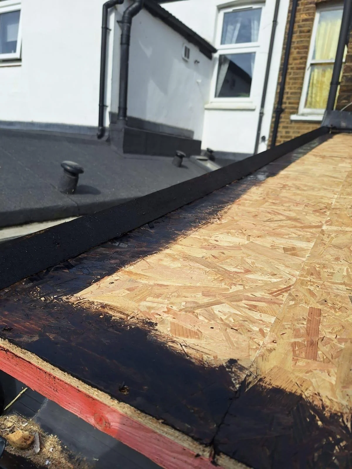 Close-up view of a roof under construction showing plywood sheathing with black protective coating along the edge.