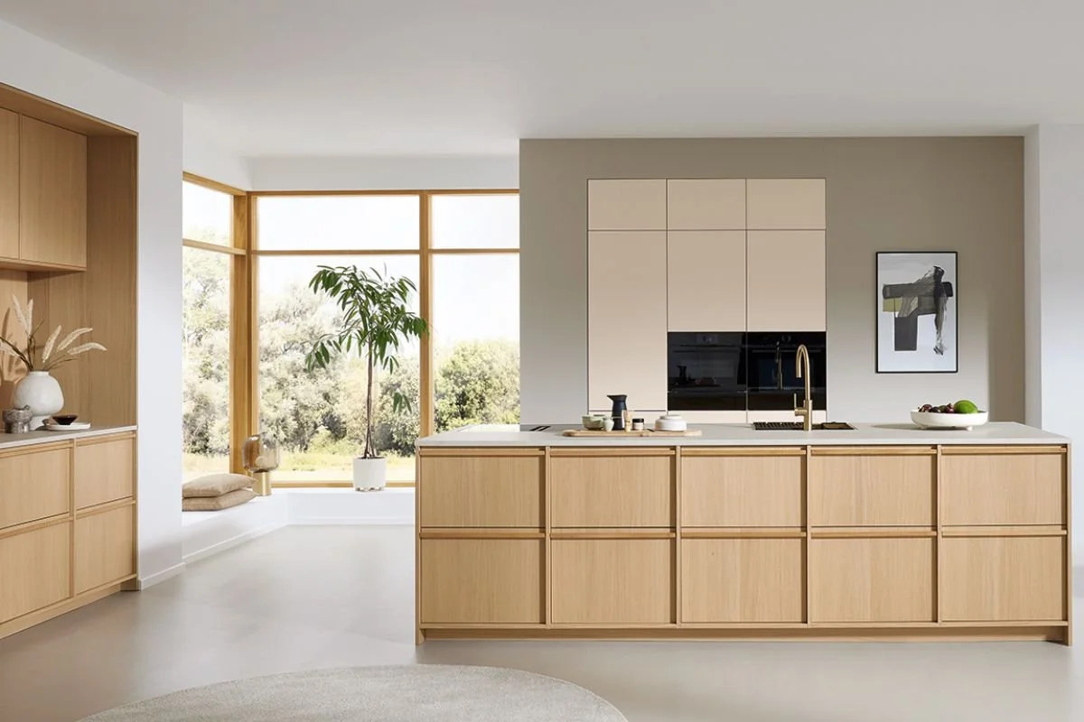 Cuisine moderne avec îlot en bois clair, grand mur avec armoires intégrées et fenêtre panoramique avec vue sur la nature.