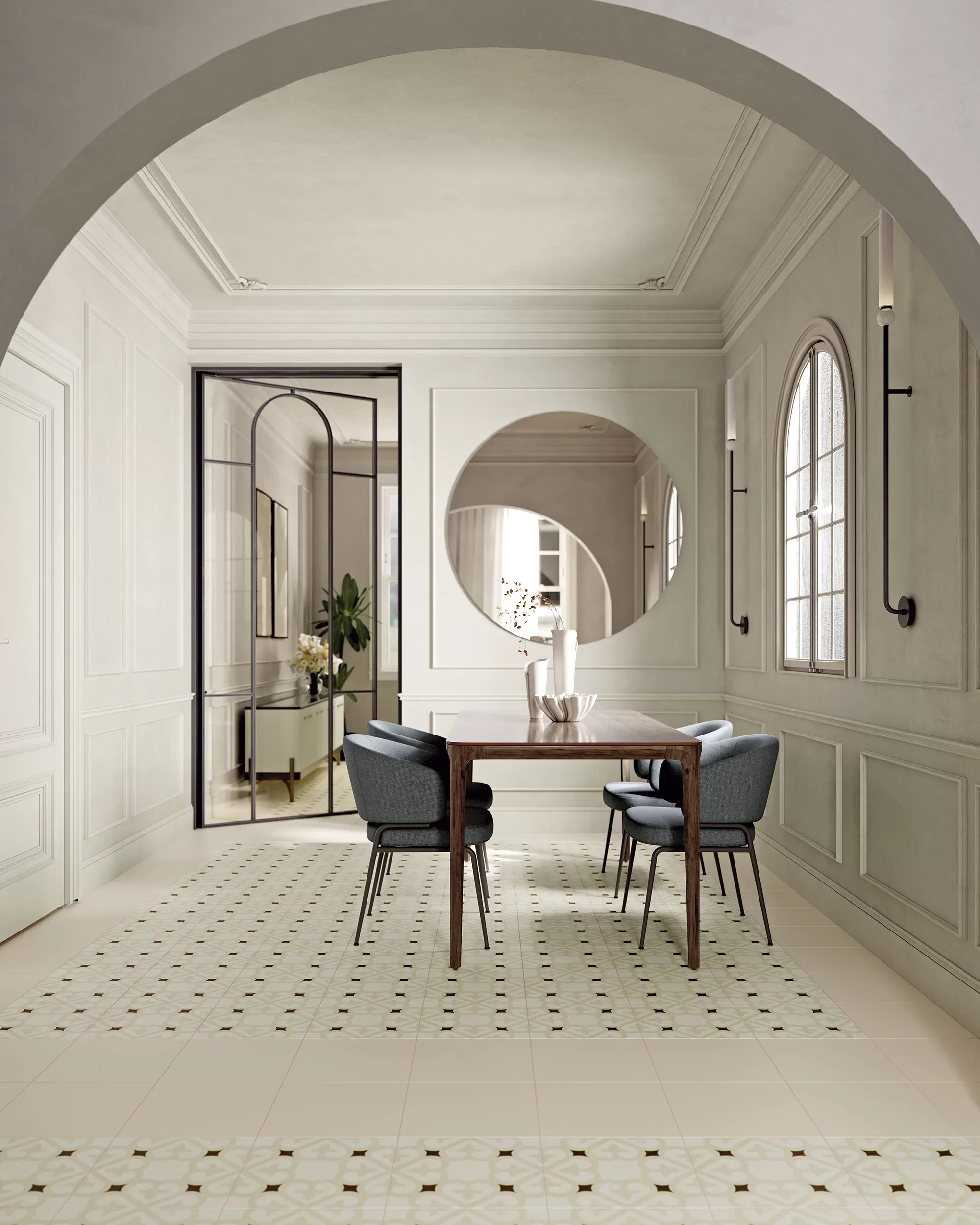 Salle à manger élégante avec table en bois, six chaises en tissu gris et miroir rond mural, dans un intérieur lumineux avec fenêtres arquées.
