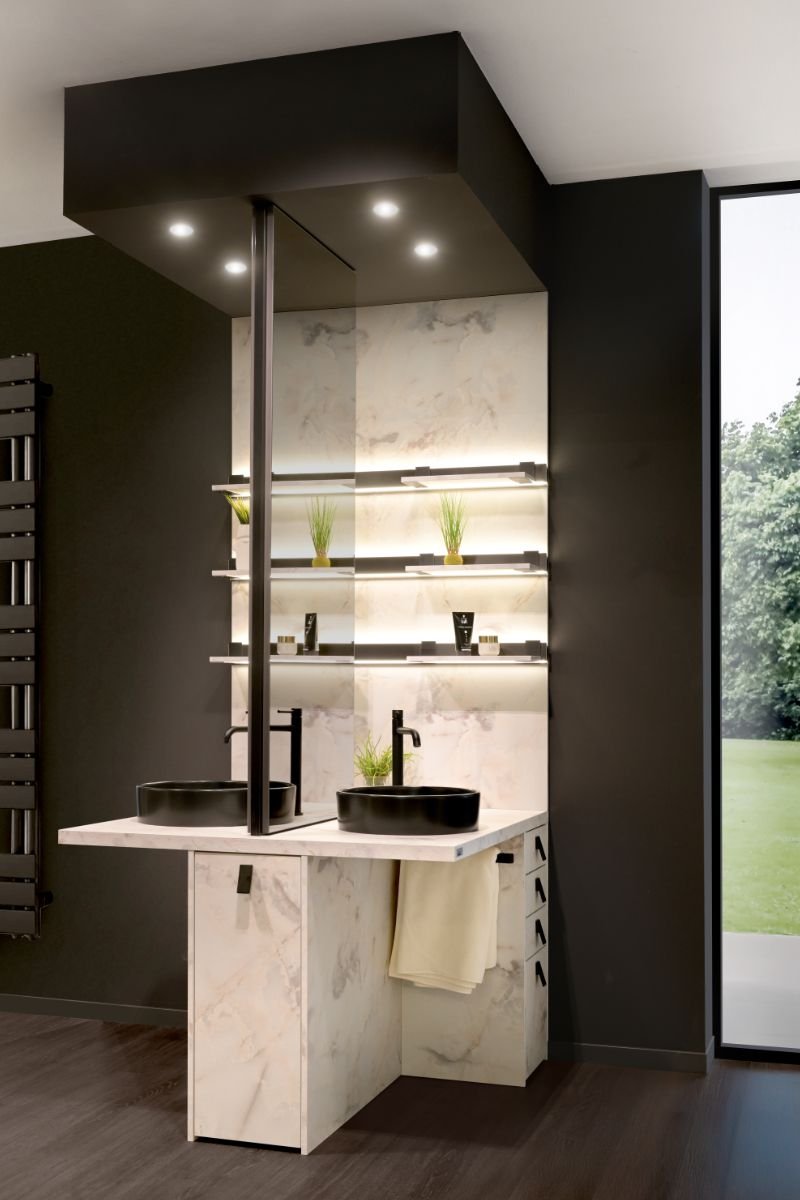 Intérieur moderne avec un meuble en marbre blanc, deux lavabos noirs, étagères éclairées avec des plantes vertes, et une grande fenêtre offrant une vue sur un extérieur verdoyant.