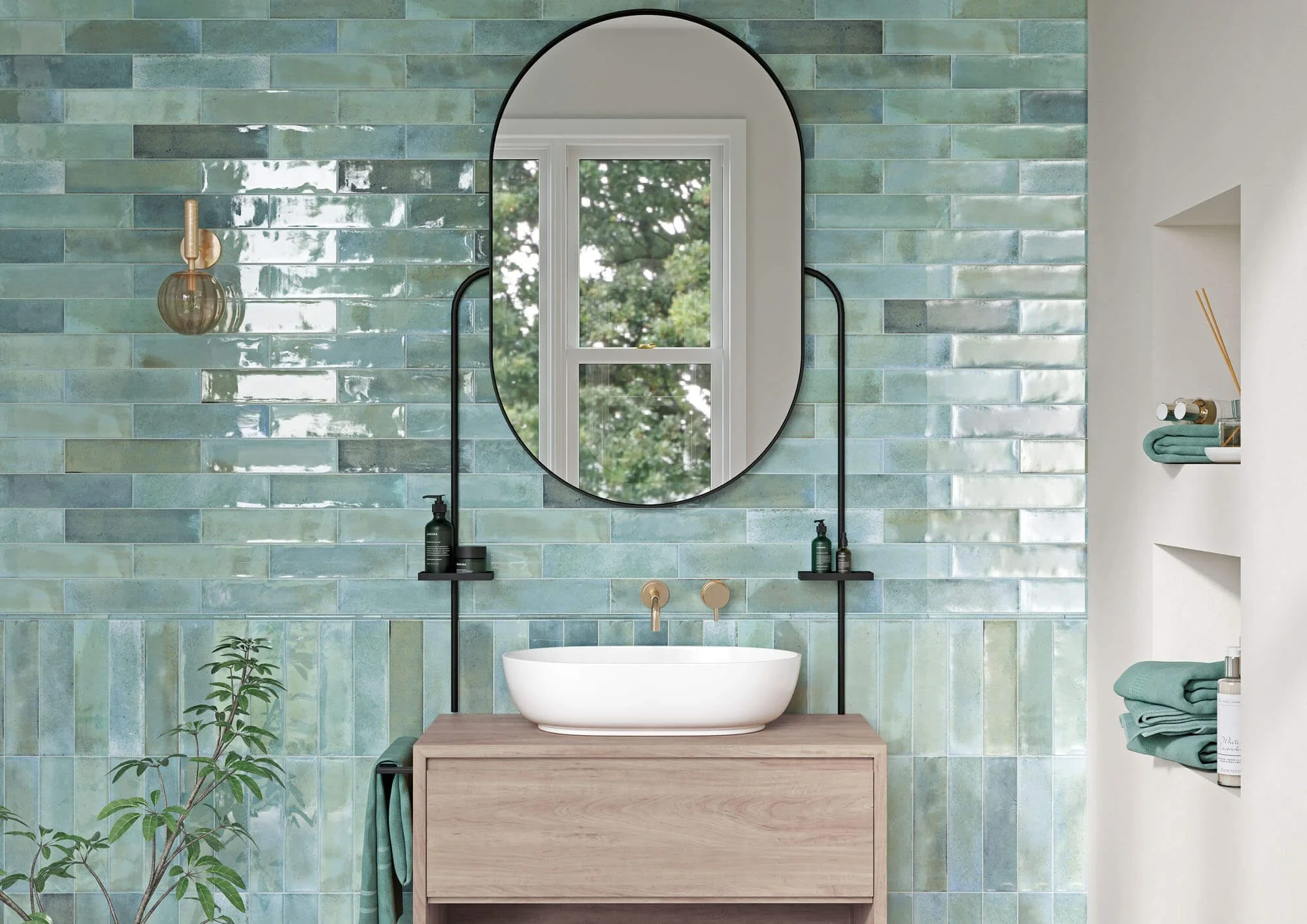 Salle de bain moderne avec mur en carreaux de céramique vert et miroir oval, lavabo blanc sur une unité en bois, étagères avec serviettes et produits de soin.