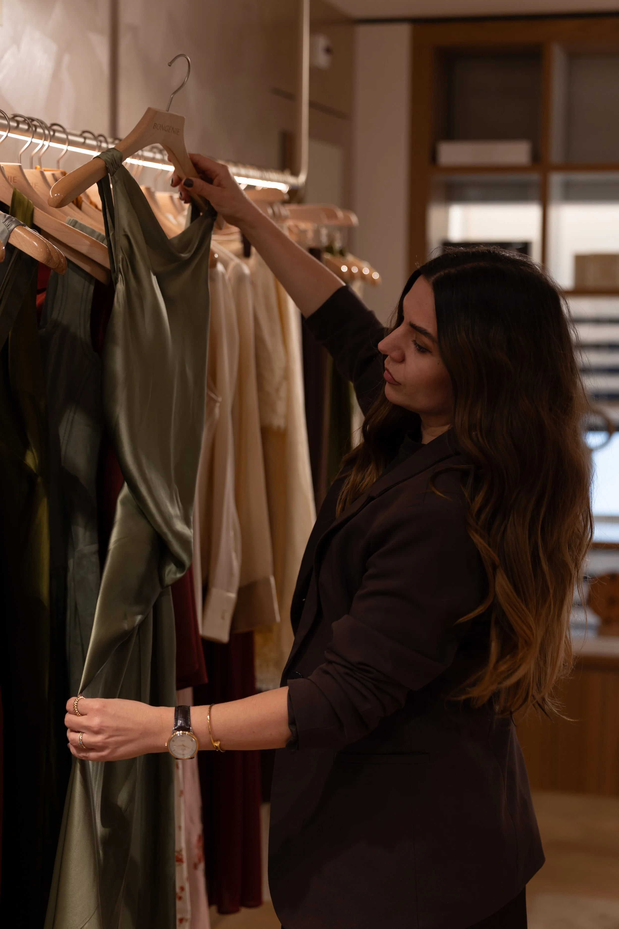 Woman shopping for dresses in a boutique store, holding a satin dress on a hanger.