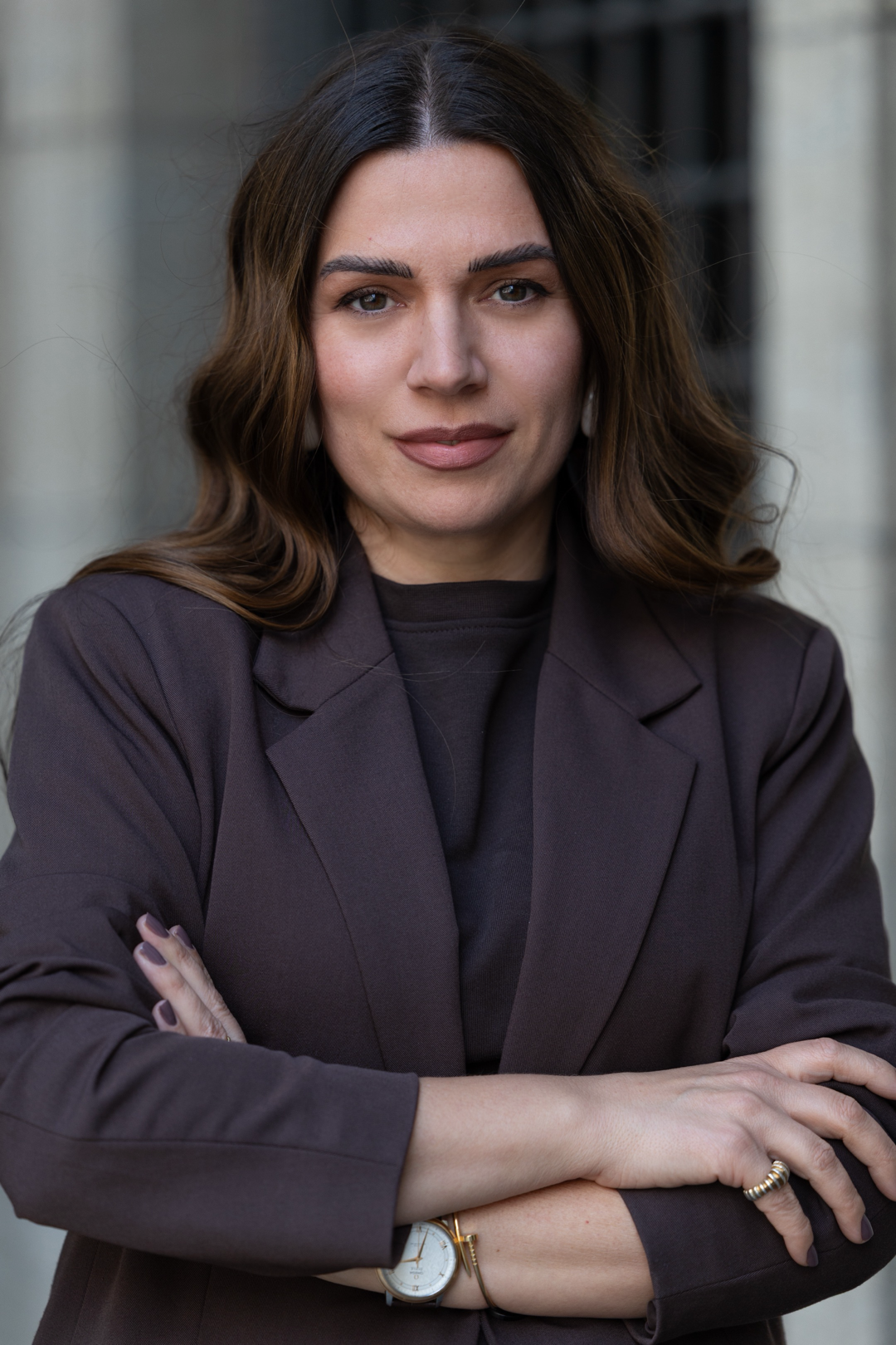 A woman with brown hair, wearing a dark blazer, standing outdoors with her arms crossed.
