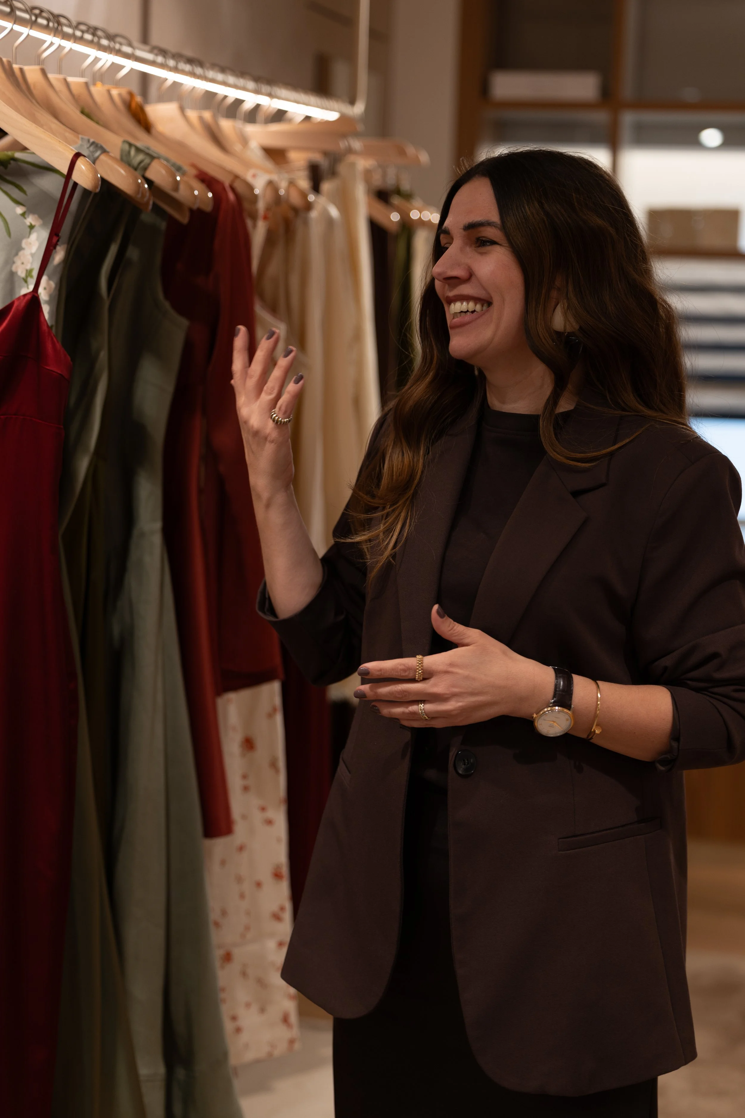 A woman shopping for dresses on a clothing rack, smiling and touching a maroon dress.