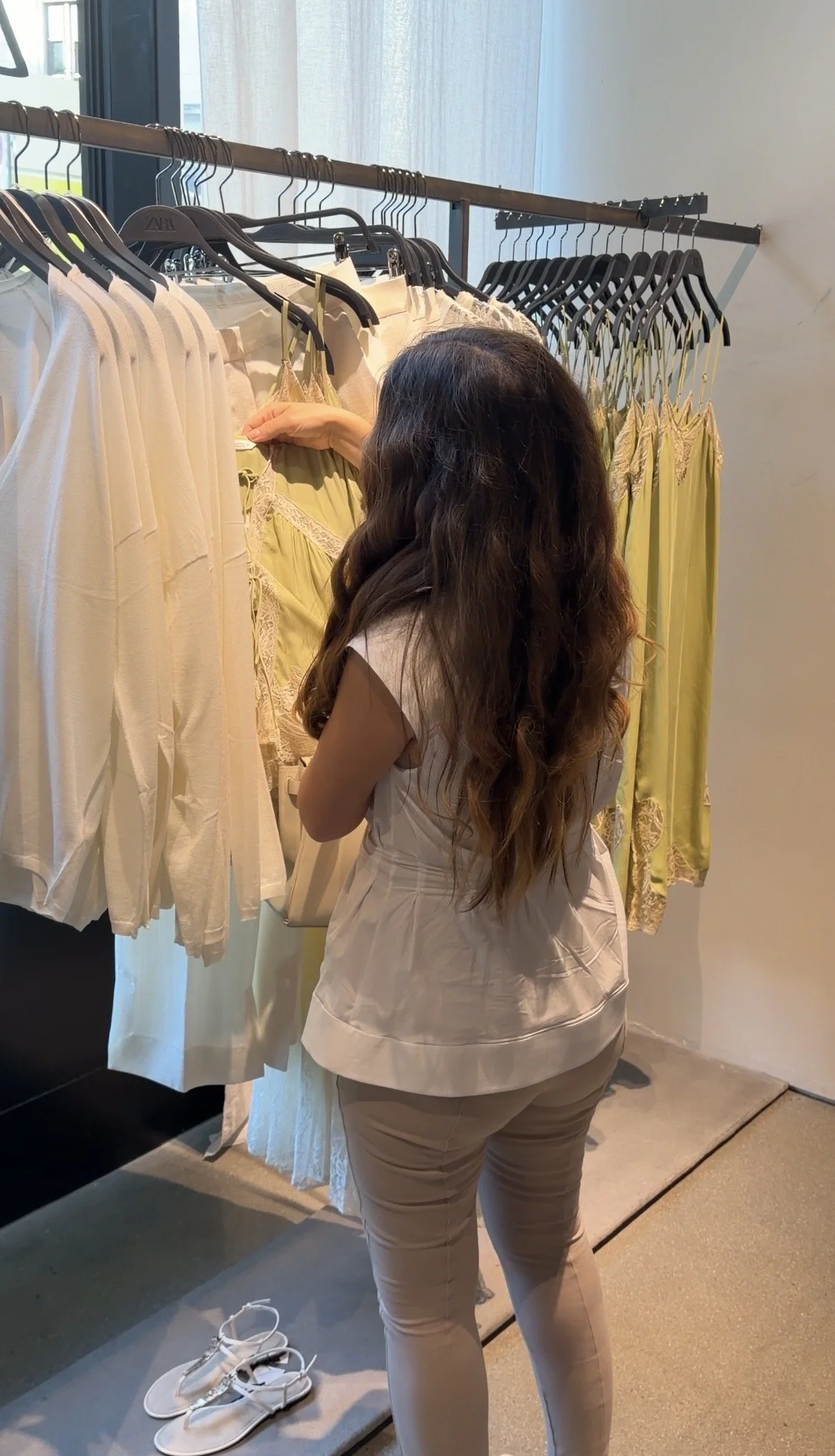 A woman shopping for clothes, examining yellow and white dresses on a rack in a clothing store.