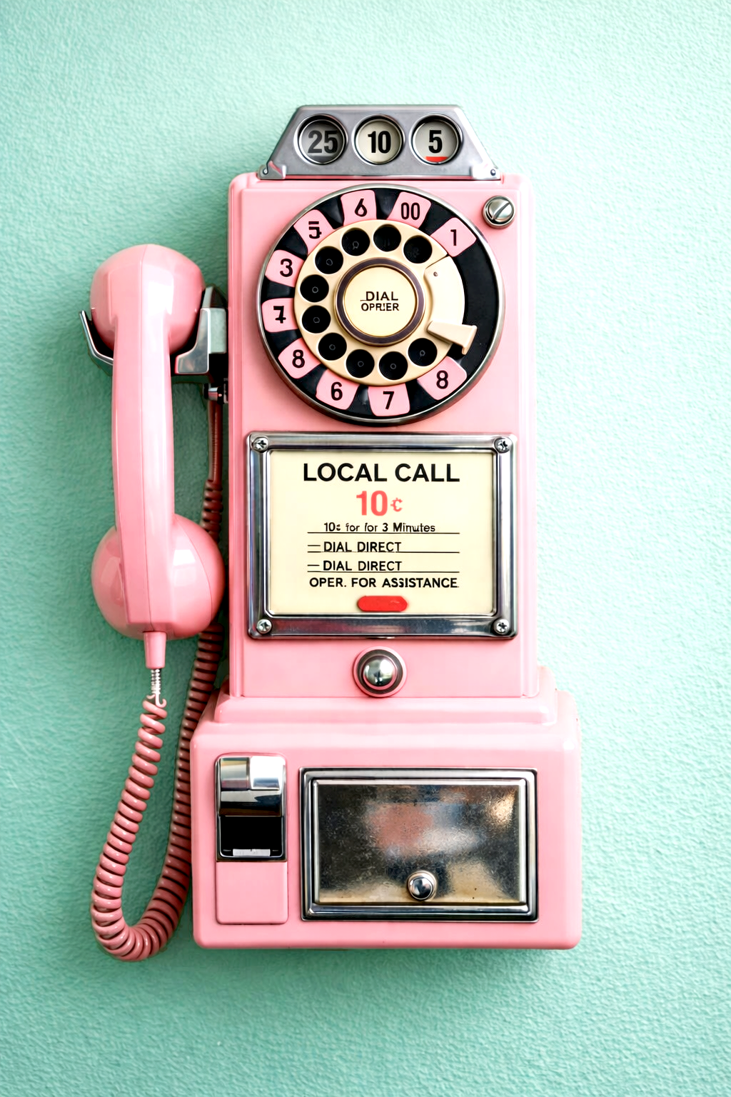 A pink vintage payphone mounted on a green wall.