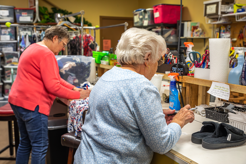 Two women working at a worktable and pricing donations for the Thrift Shop.