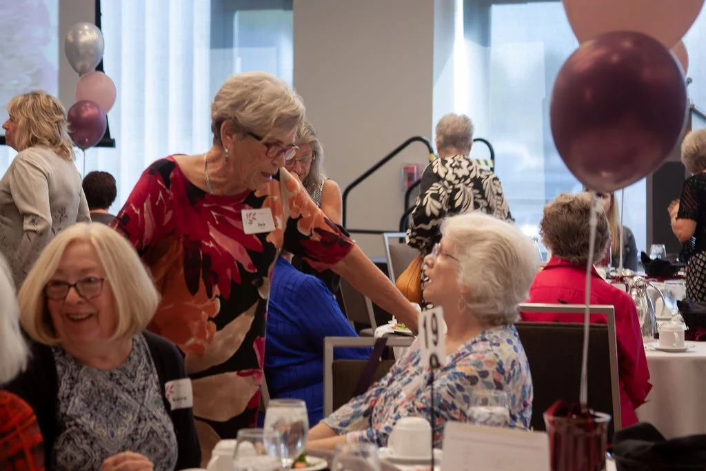 Women socializing at a banquet table decorated with balloons, during a celebration event.