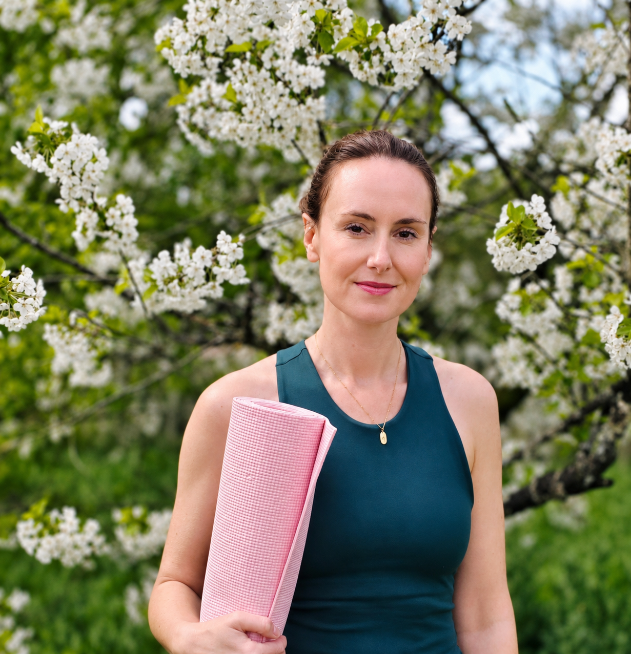 Jenny Hopps Pilates, standing by a blossom tree with a pink pilates mat