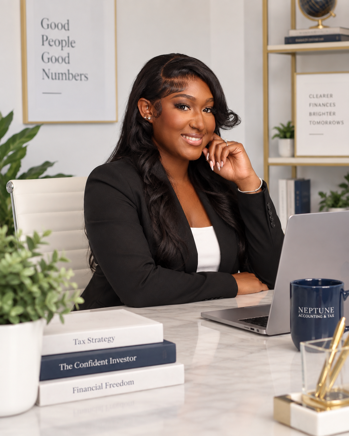 A professional woman sitting at a desk in an office, smiling, wearing a black blazer. There are books about finance and investment on the desk, a laptop, a plant, and office decor in the background.