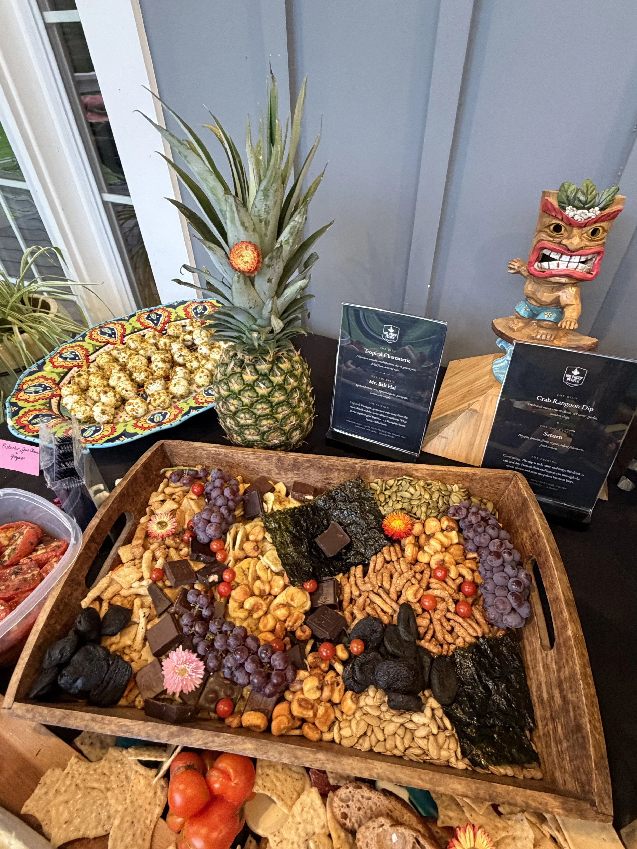 Tropical charcuterie spread featuring fruit, snacks, chocolates, and roasted tomatoes.
