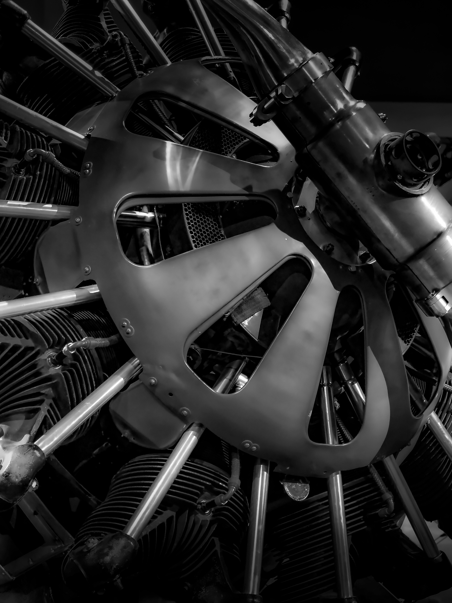 Close-up of a vintage military aircraft engine with various metal components, cooling fins, and structural supports in black and white.