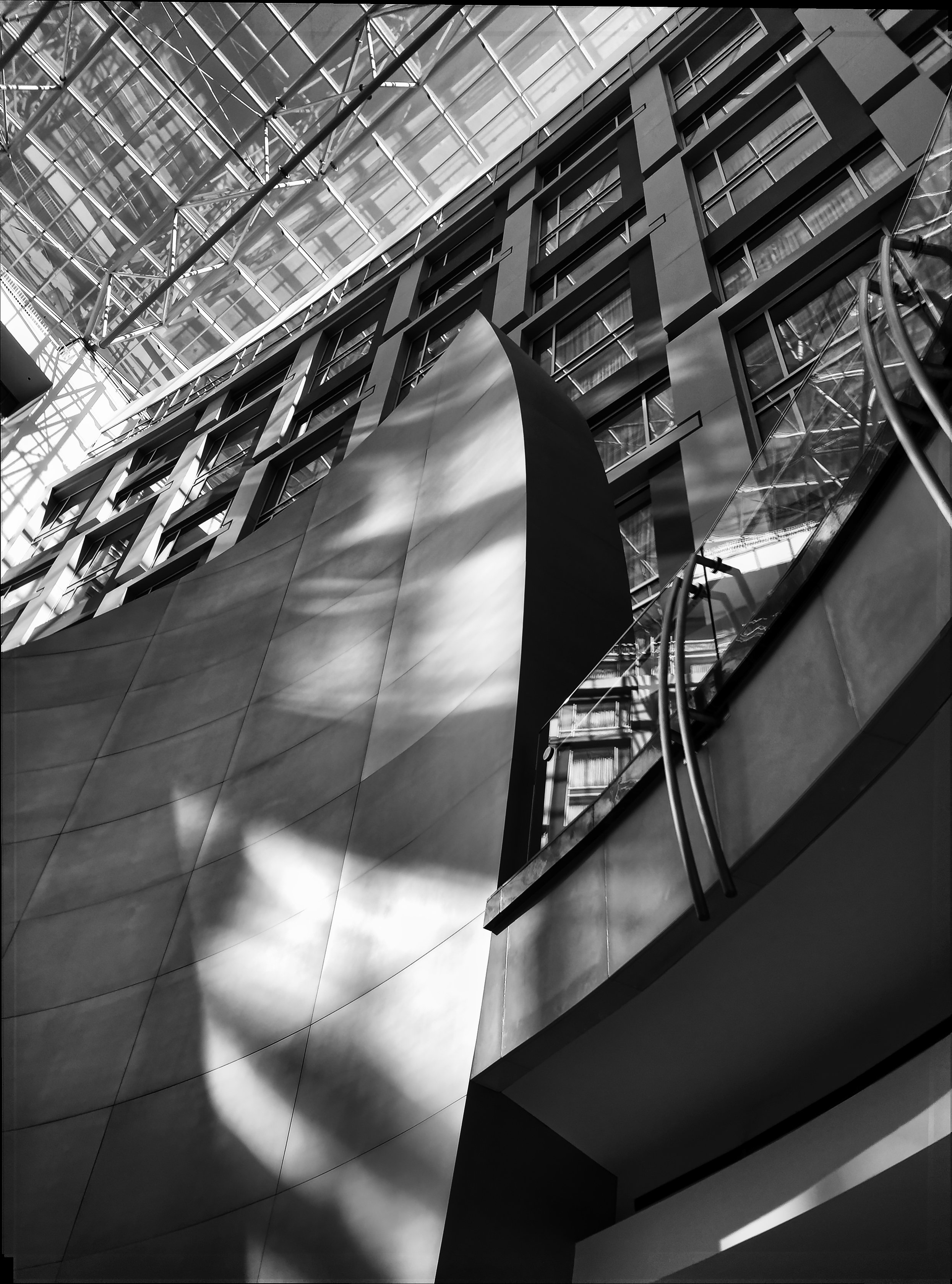 Black and white photo of modern architectural building with glass and metal facade, capturing geometric shapes and reflections.