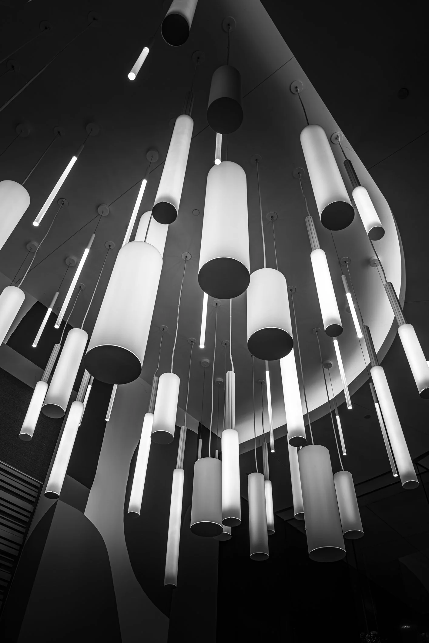 Stylish black-and-white modern space with numerous hanging cylindrical pendant lights varying in size, creating a dynamic chandelier.